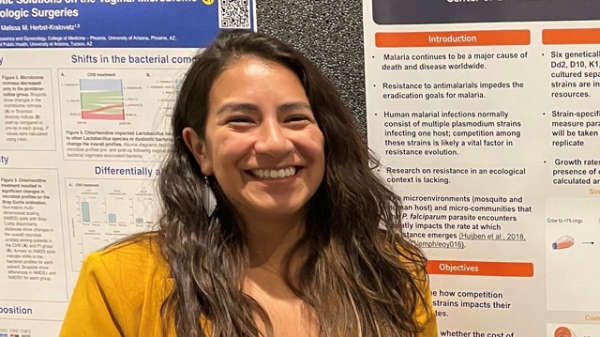 A woman smiling in front of a research poster.
